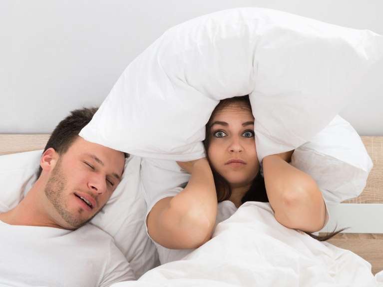 man snoring while woman is covering her ears with pillow